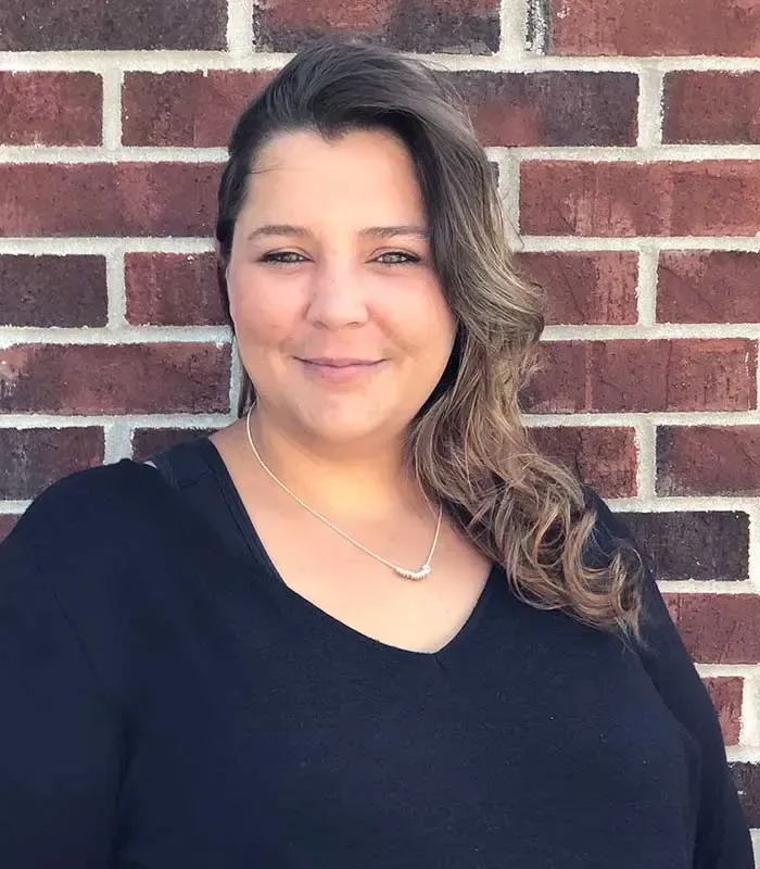 A woman in a black shirt is standing in front of a brick wall.