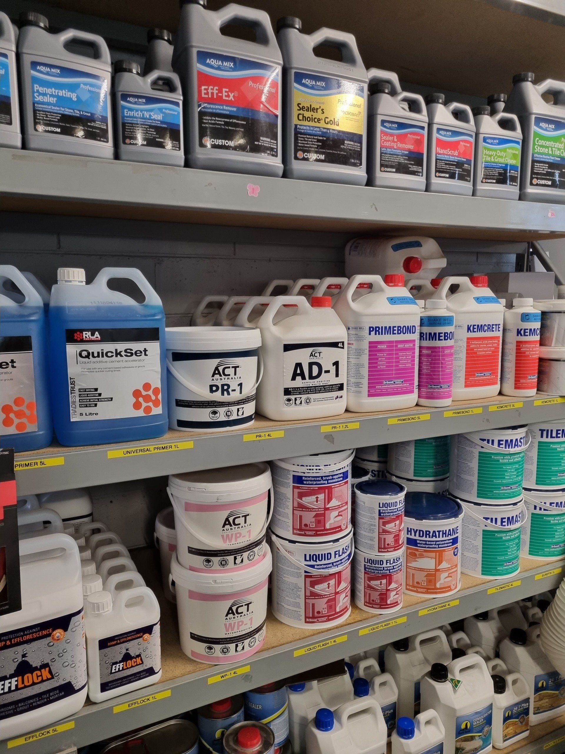 A shelf filled with lots of bottles and buckets of tiles supplies.