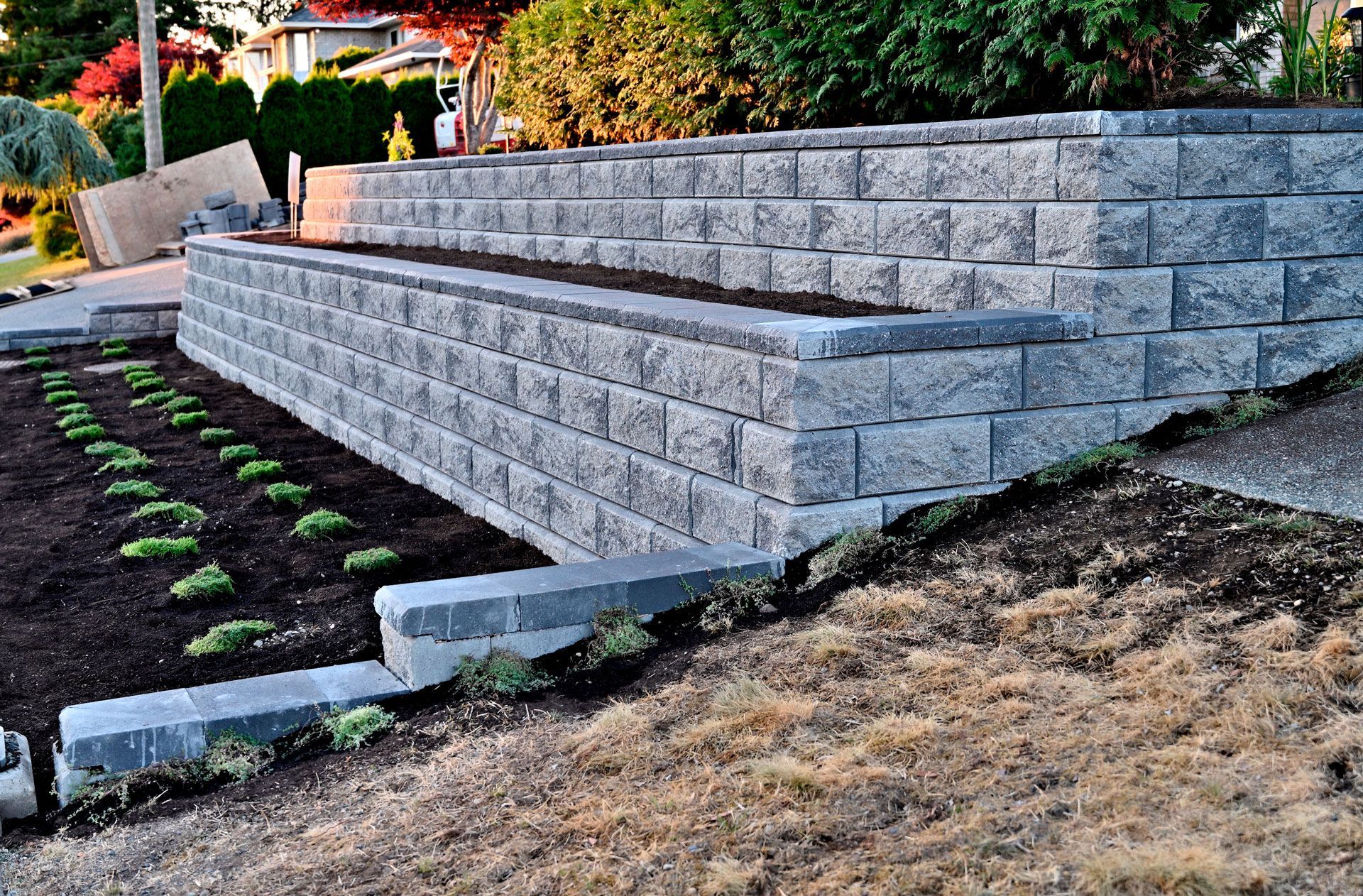 Tiered gray stone retaining walls beside a landscaped slope with newly planted greenery and mulch