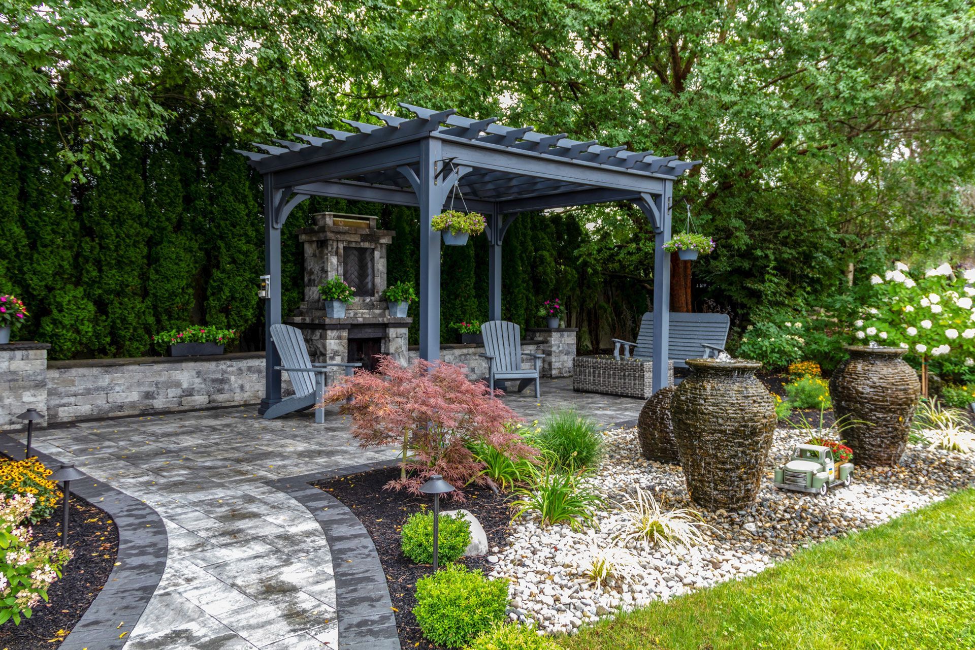 Stone garden path leading to a dark gray pergola in a lush backyard garden with shrubs and trees