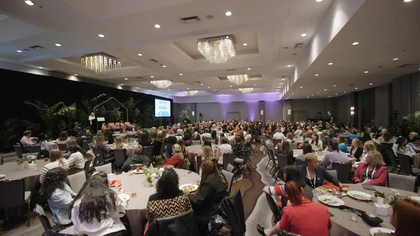 Large event hall with many people seated at round tables.