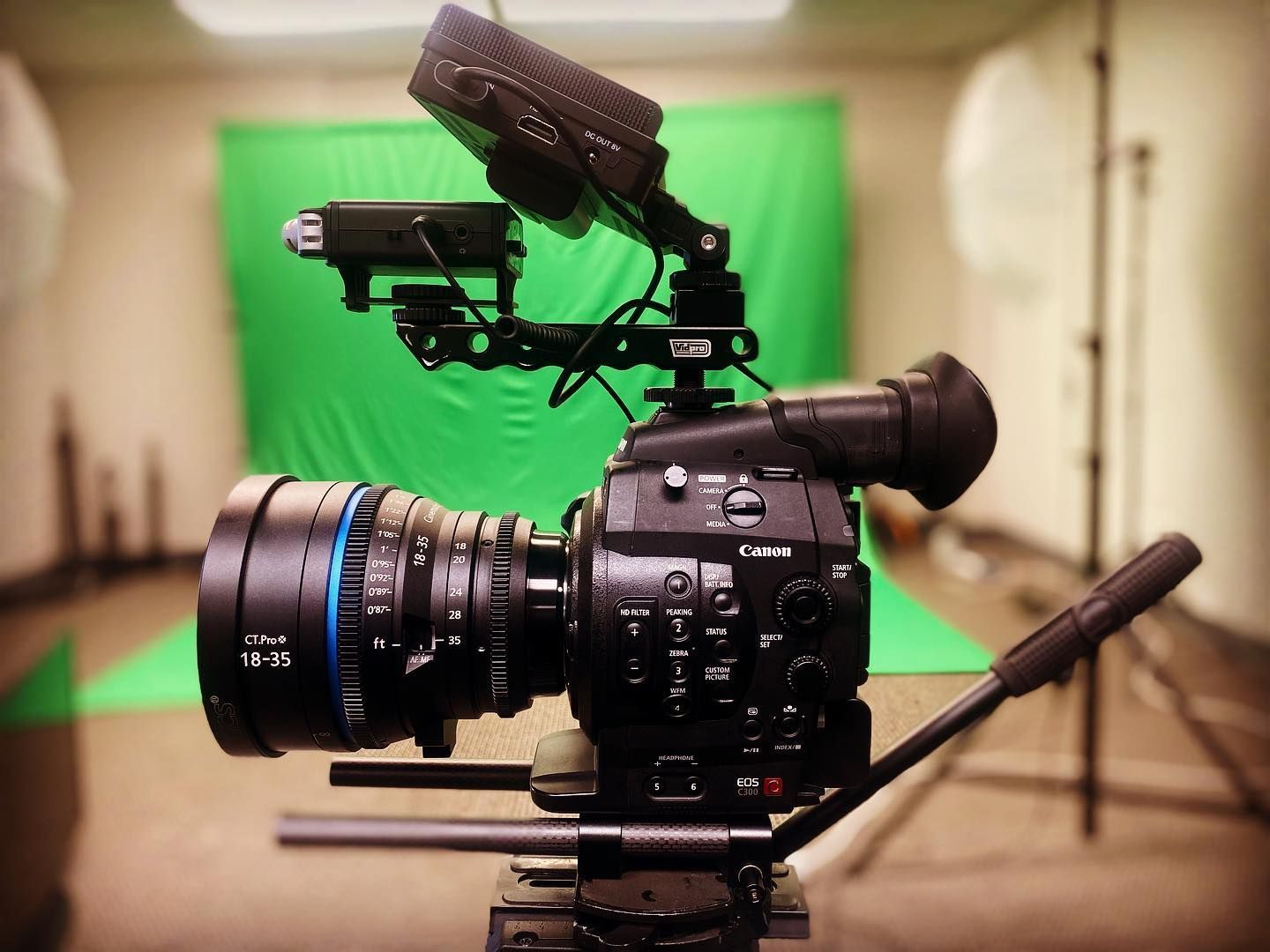 Video camera on tripod in a studio, with green screen background.