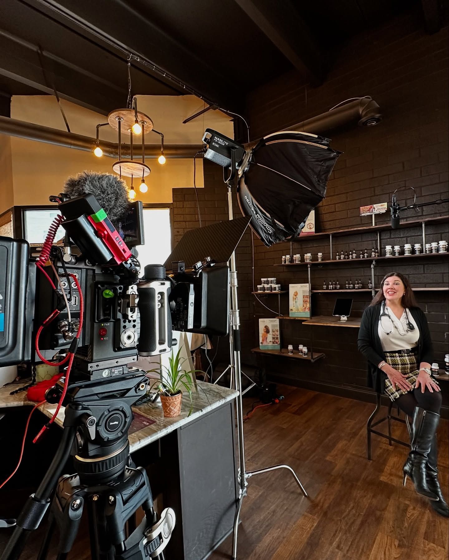Camera filming woman in a retail space with black brick wall and softbox lighting.
