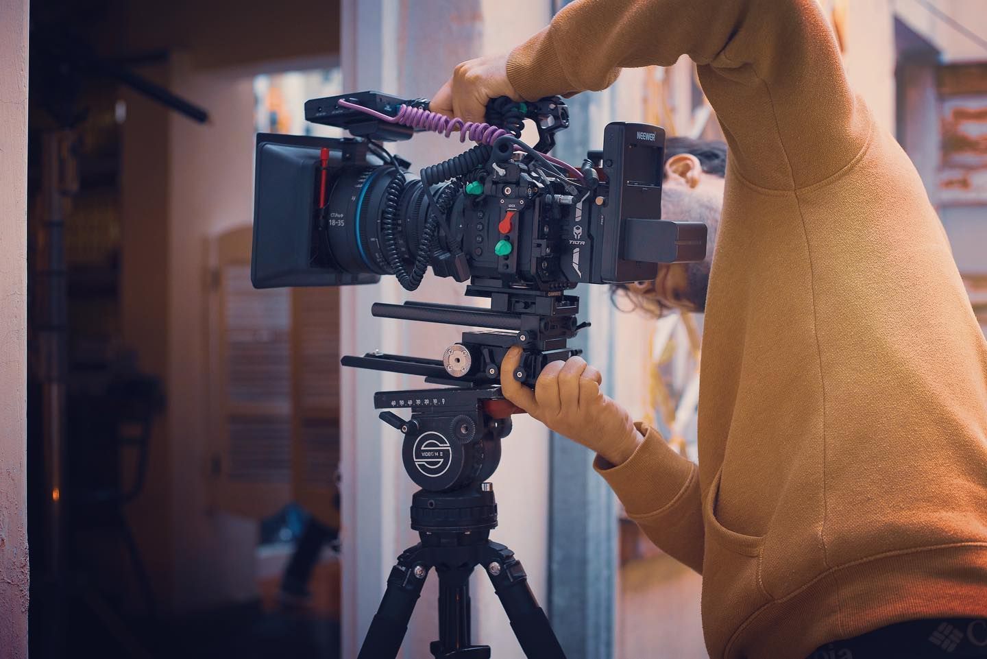 Person adjusting a professional video camera mounted on a tripod inside a building.