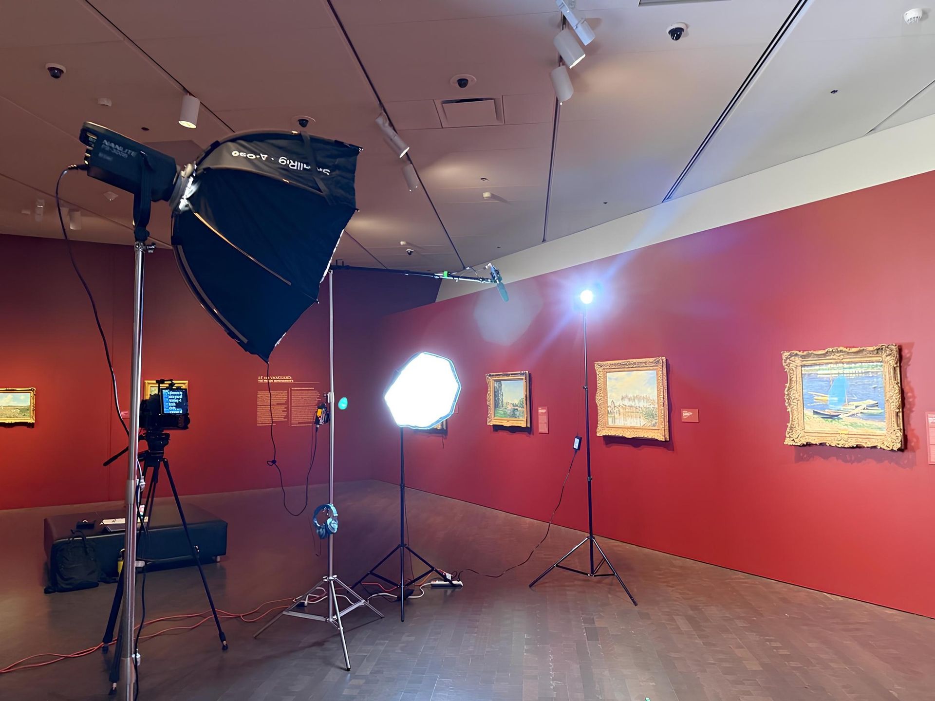 Equipment set up in a museum gallery to photograph paintings on red walls.