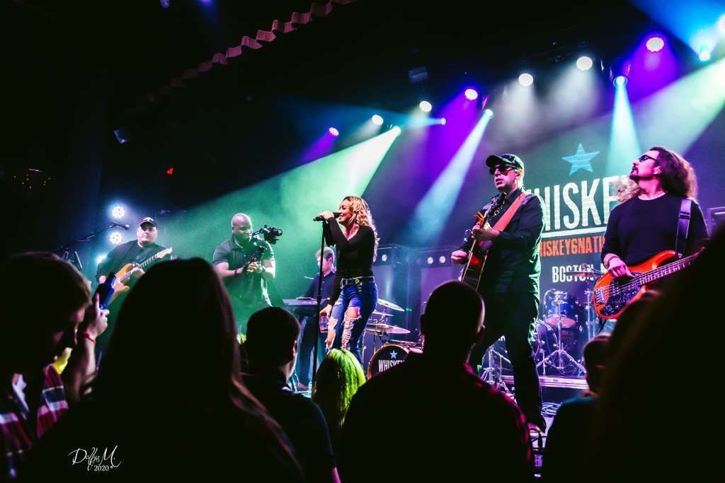 Band performing on stage with colorful lights, audience in foreground.