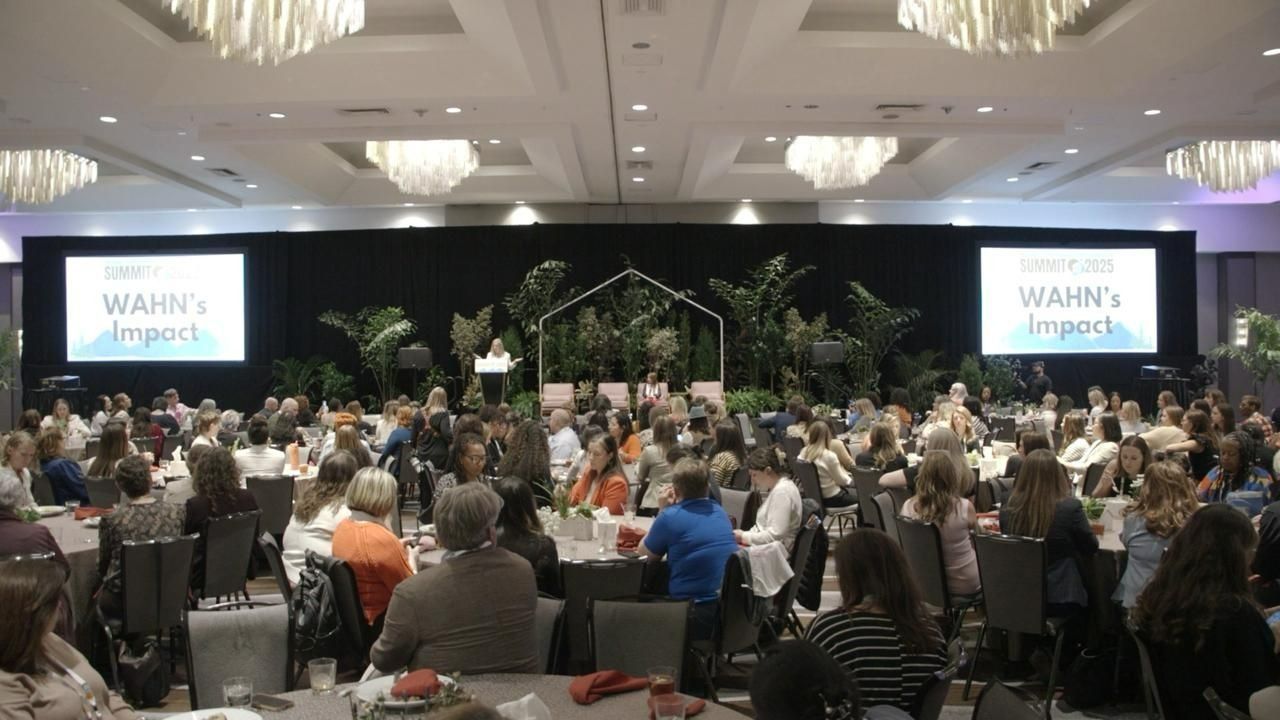 Large conference hall with audience facing stage with screens. 