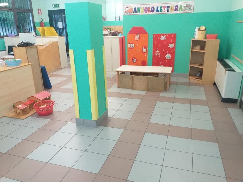 Sala giochi vuota con colonna colorata e mobili per bambini; pareti verde chiaro, pavimento decorato.
