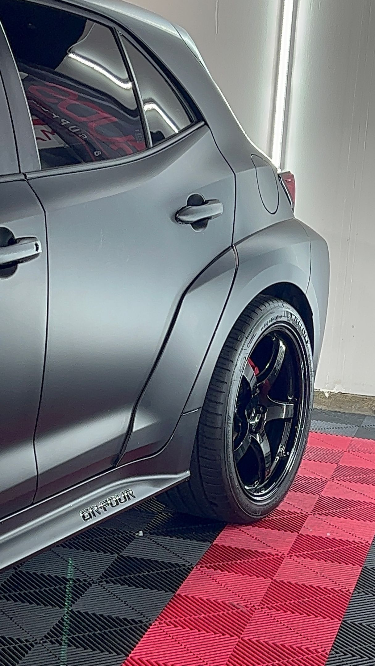A black car is parked on a red mat in a garage.