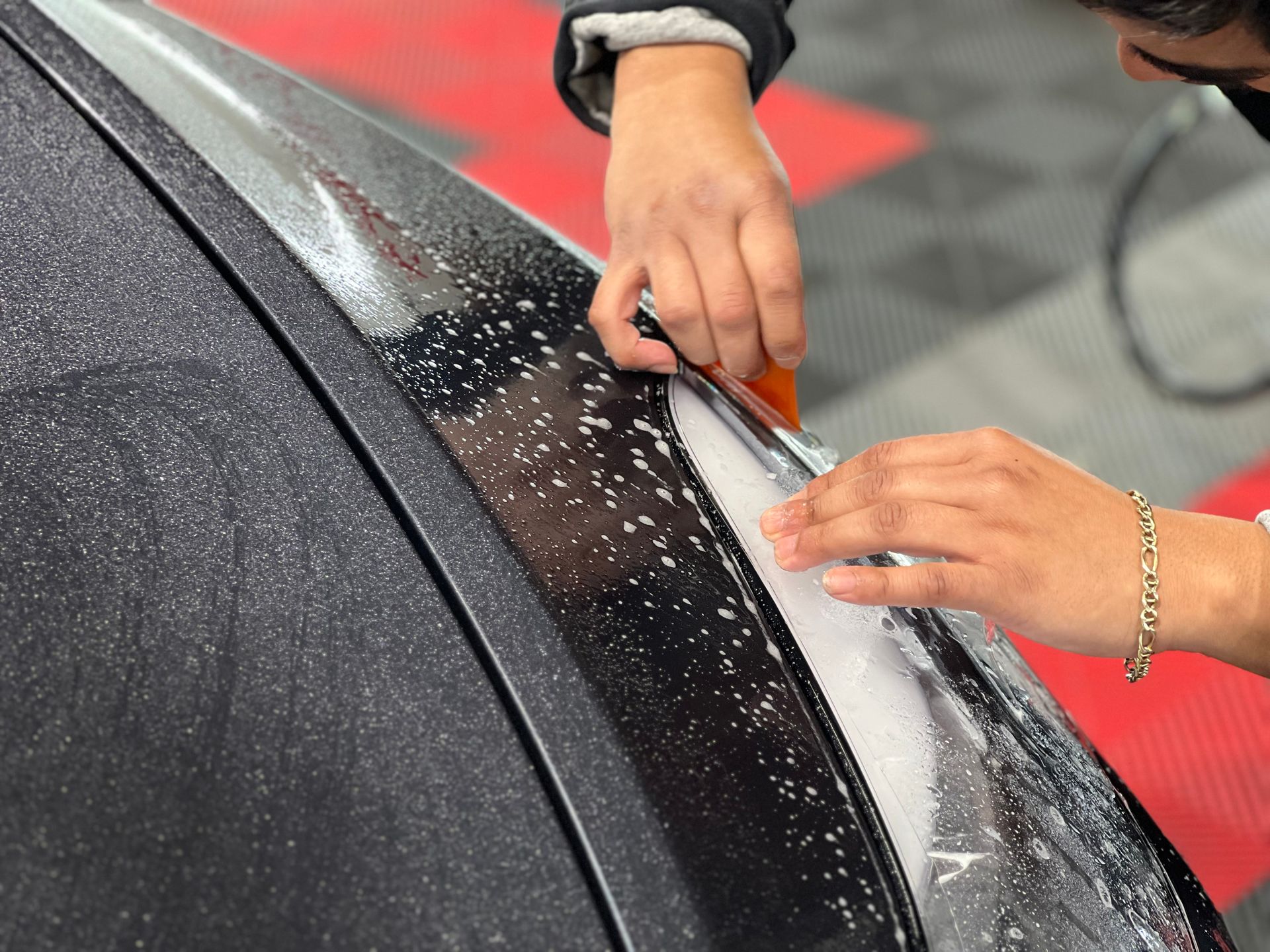 A person is applying a clear film to the side of a car.