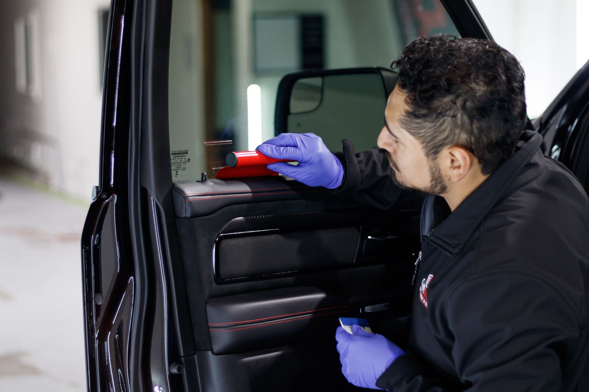 A man in a black jacket and purple gloves is cleaning the door of a car.