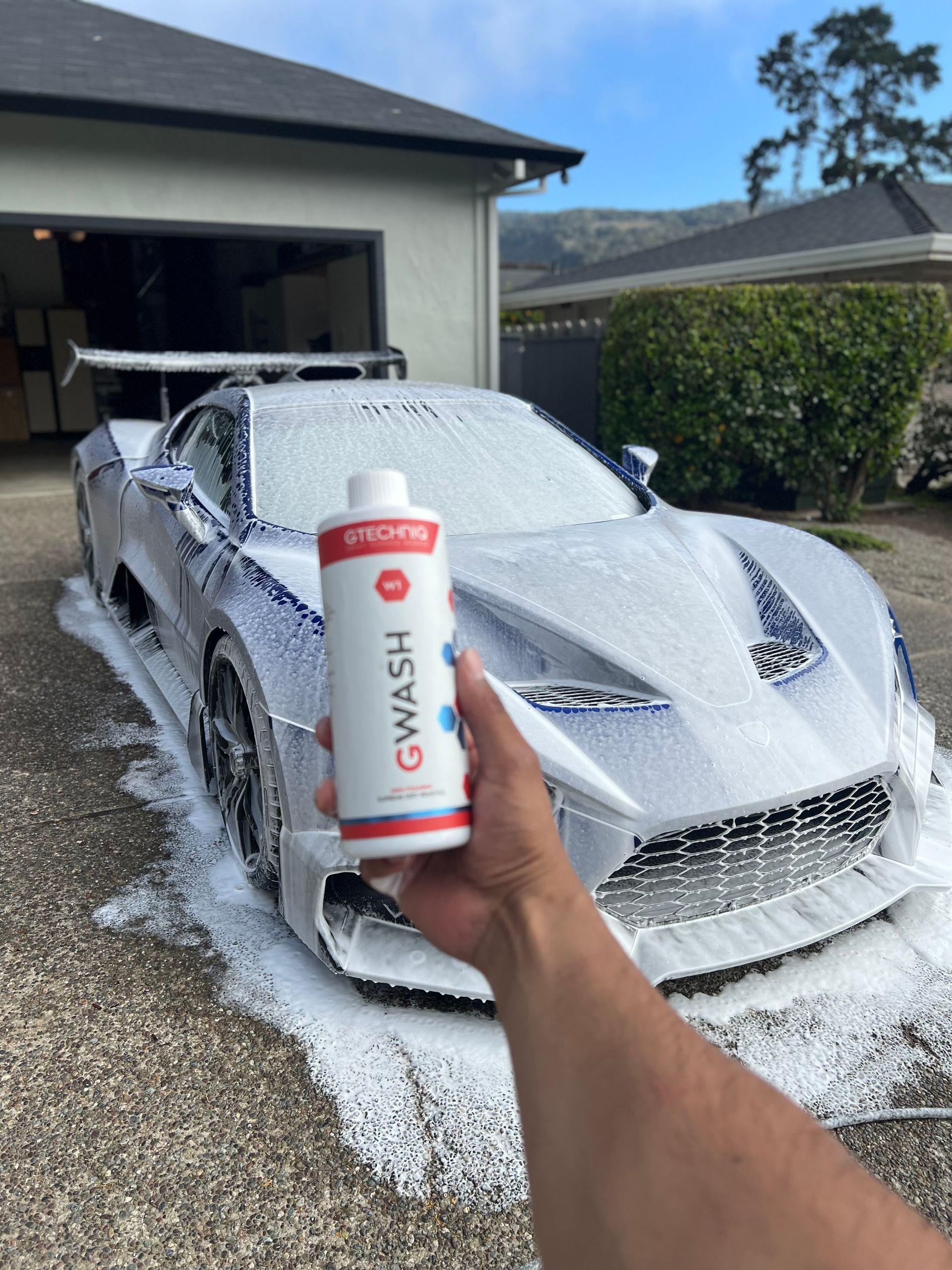 A person is holding a bottle of gwash in front of a car