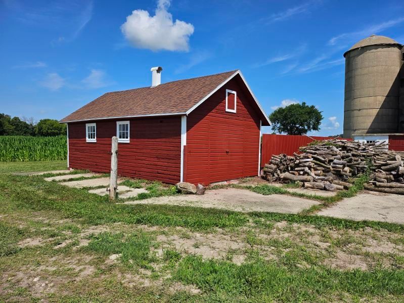 A red barn is sitting in the middle of a grassy field next to a silo.