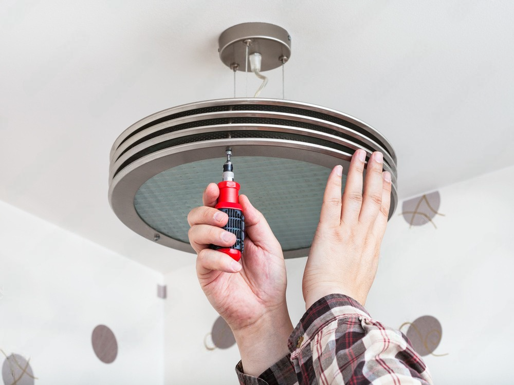 a person is fixing a light fixture with a screwdriver