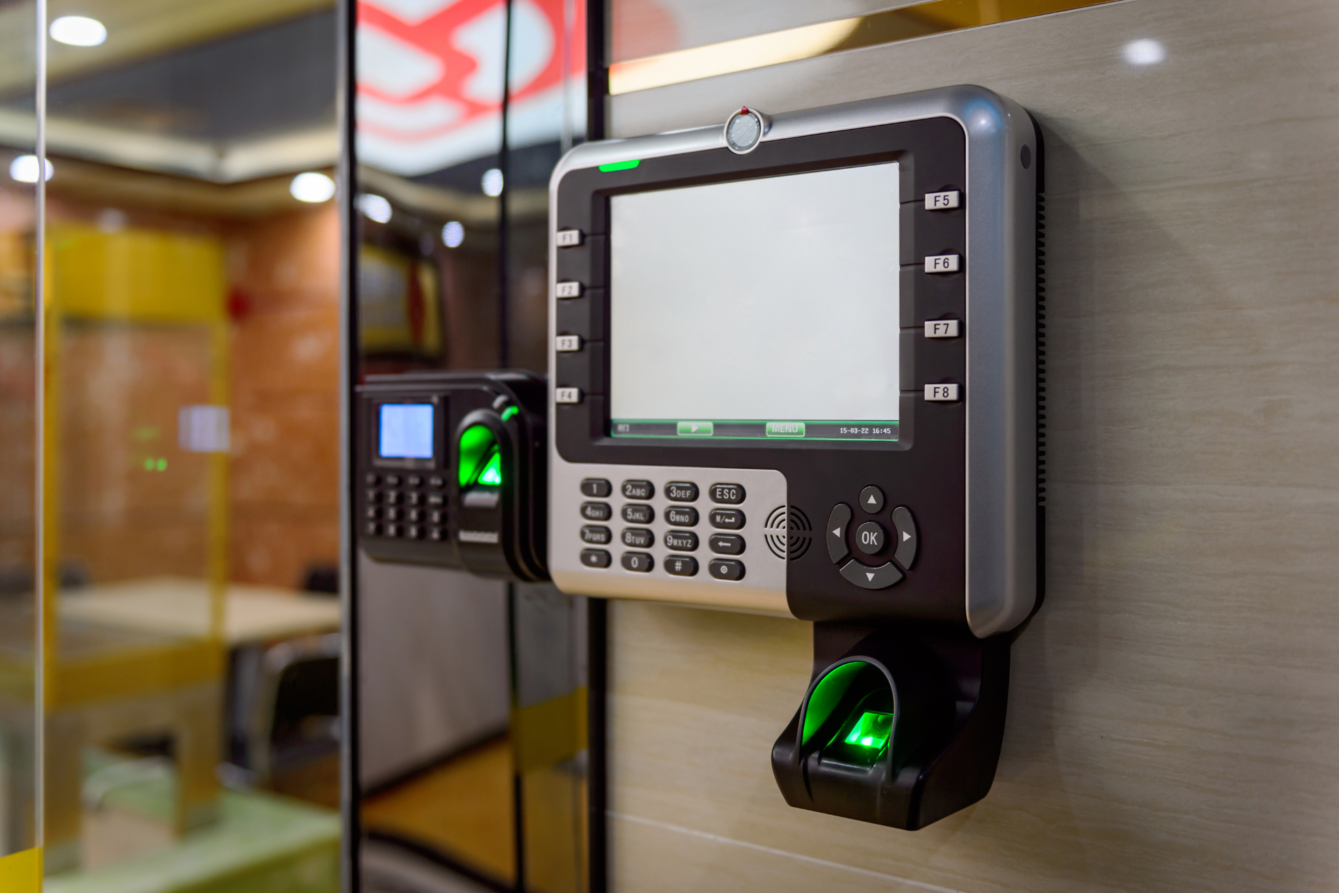 A fingerprint scanner is mounted on a wall in a building.