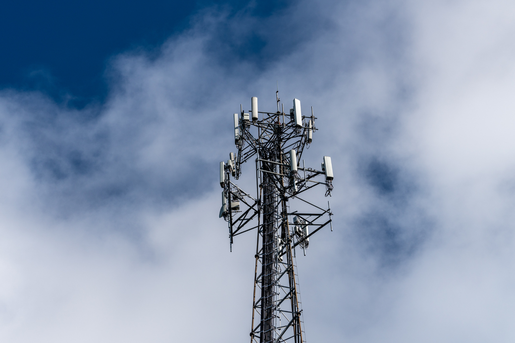 A telephone tower with antennas against a cloudy blue sky.