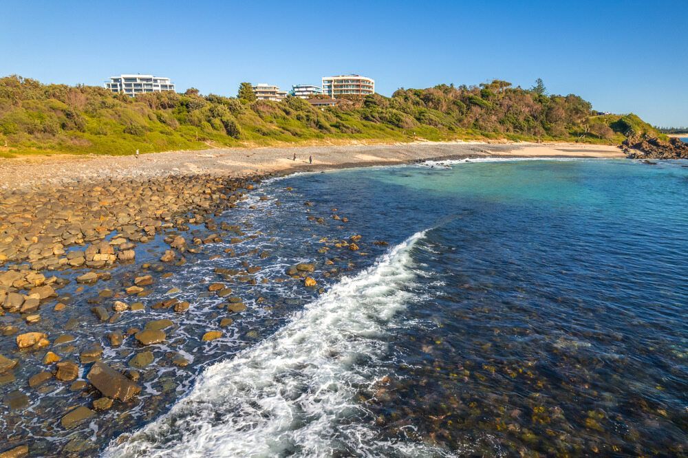 Rocky Beach With Turquoise Water, Green Foliage, and Buildings Under a Blue Sky — NRS Scaffolding Pty Ltd in Forster, NSW