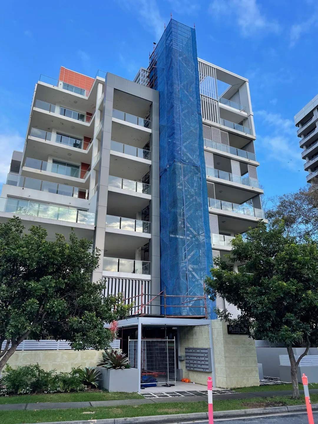 Multi-story Apartment Building With Blue Construction Netting, Trees — NRS Scaffolding Pty Ltd in Wauchope, NSW