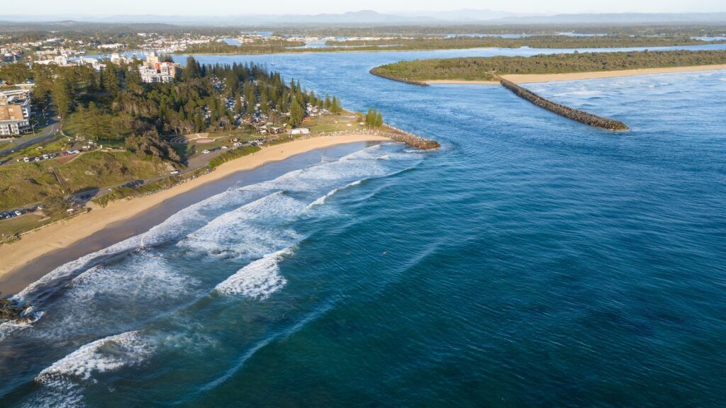 Coastal View: Beach With Waves, Grassy Shoreline, Buildings, and Ocean — NRS Scaffolding Pty Ltd in Port Macquarie, NSW