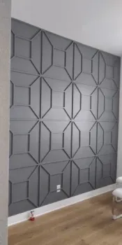 A gray accent wall featuring a repetitive, geometric, three-dimensional molding design in a room with light wood floors.