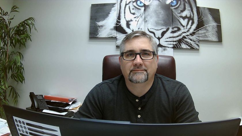 A man wearing glasses is sitting at a desk in front of a painting of a tiger.