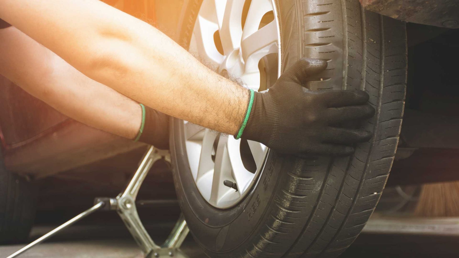A person wearing gloves changes a car tire while the vehicle is raised on a jack.