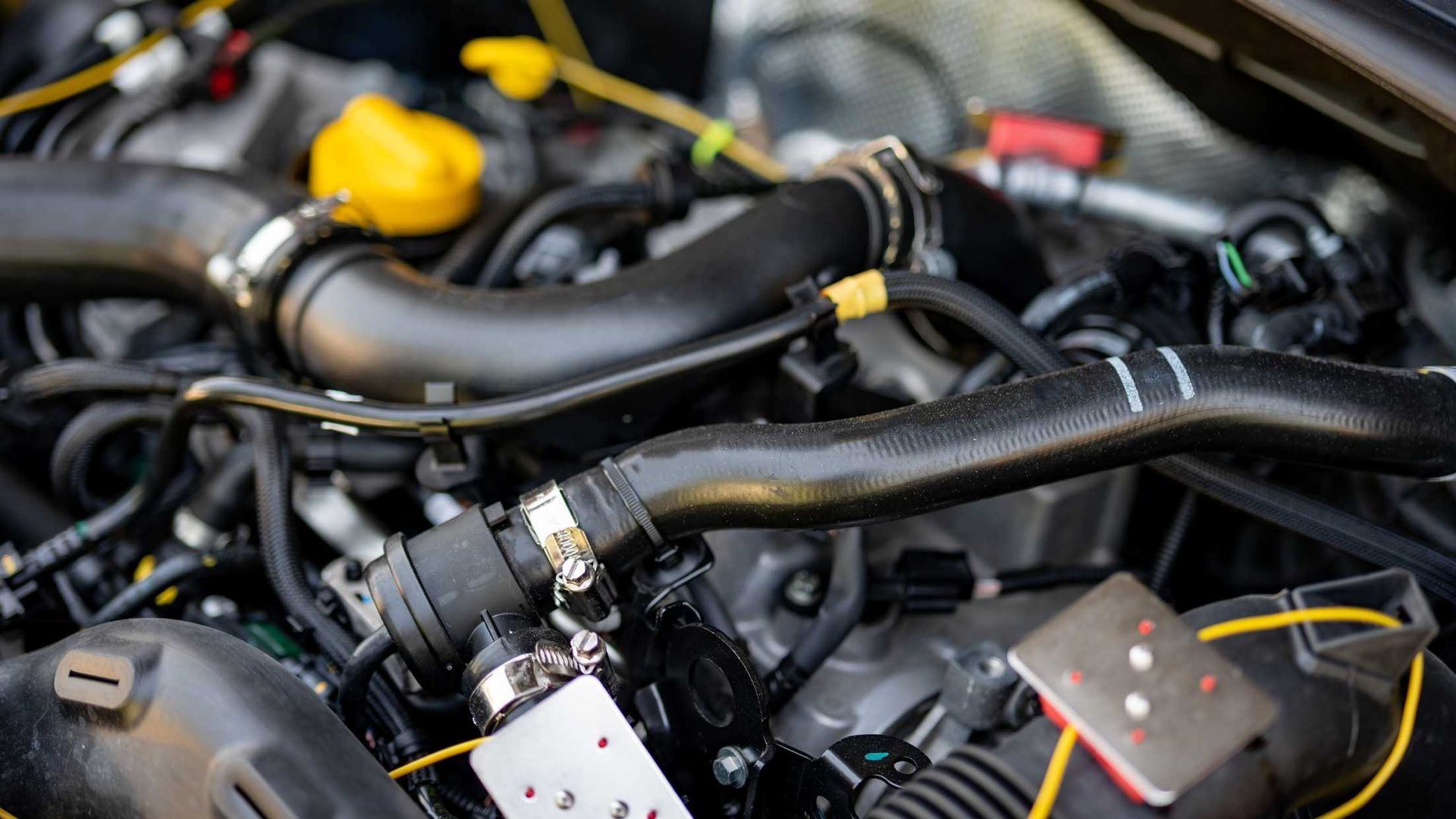 Close-up of a clean car engine bay with black rubber hoses, a yellow cap, and various mechanical components.