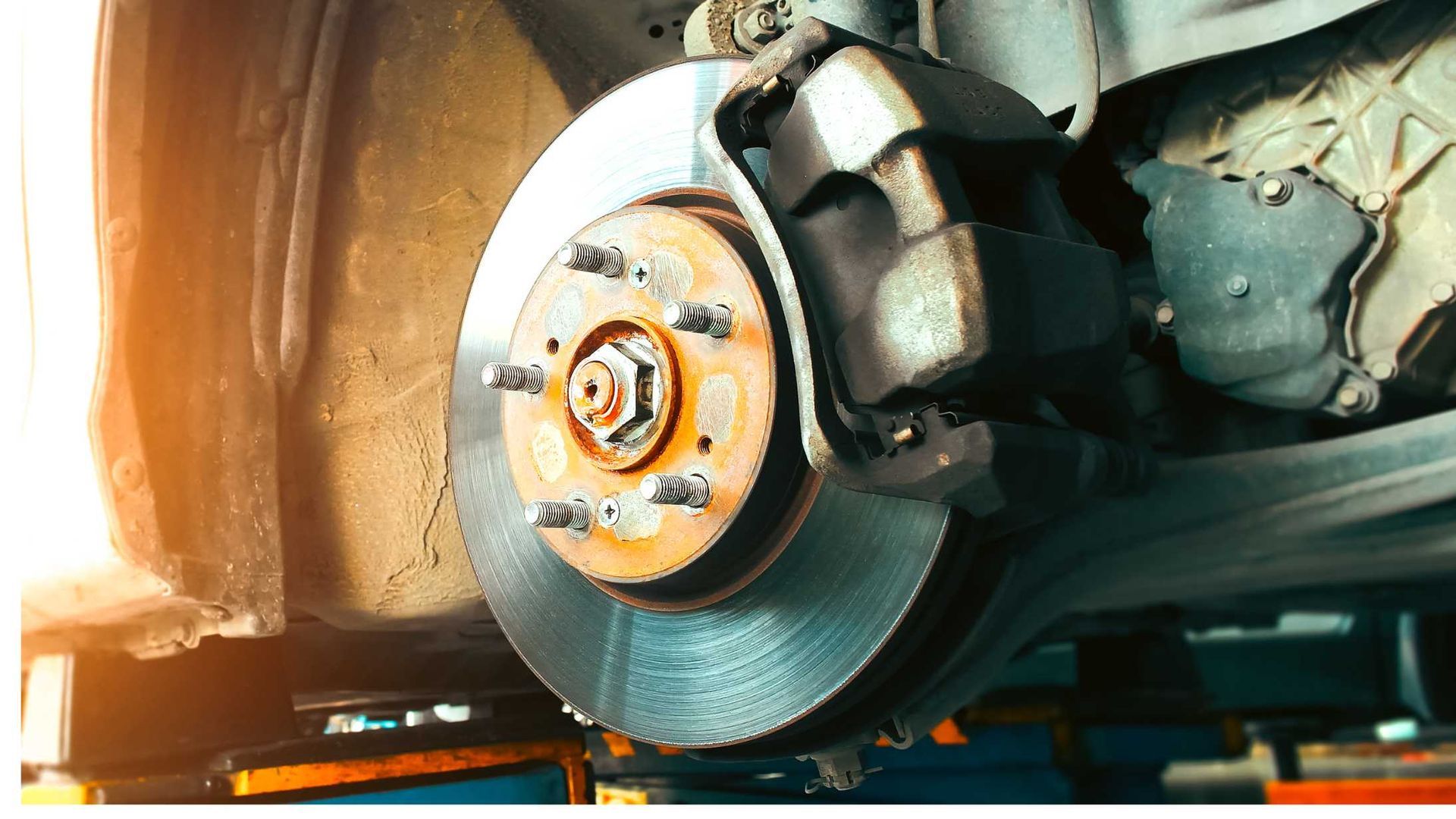 A close-up view of a car's exposed wheel hub and brake assembly, featuring a rusty brake disc and a mounted caliper.