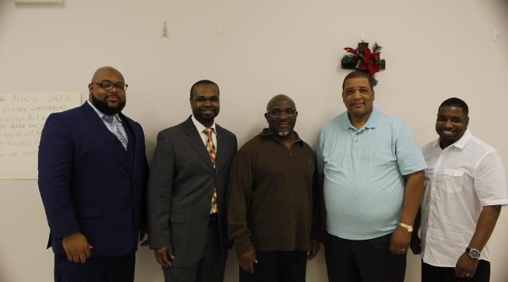 A group of men are posing for a picture in front of a white wall.