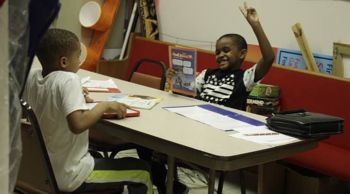 Two young boys are sitting at a table with their arms in the air