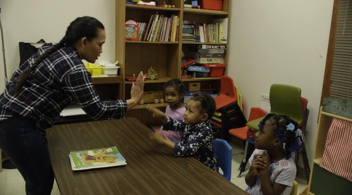 A woman is giving a high five to a group of children sitting at a table.