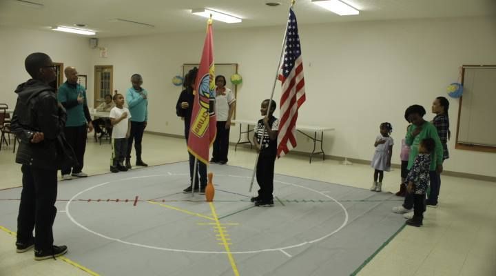 A group of people are standing around a flag in a room.