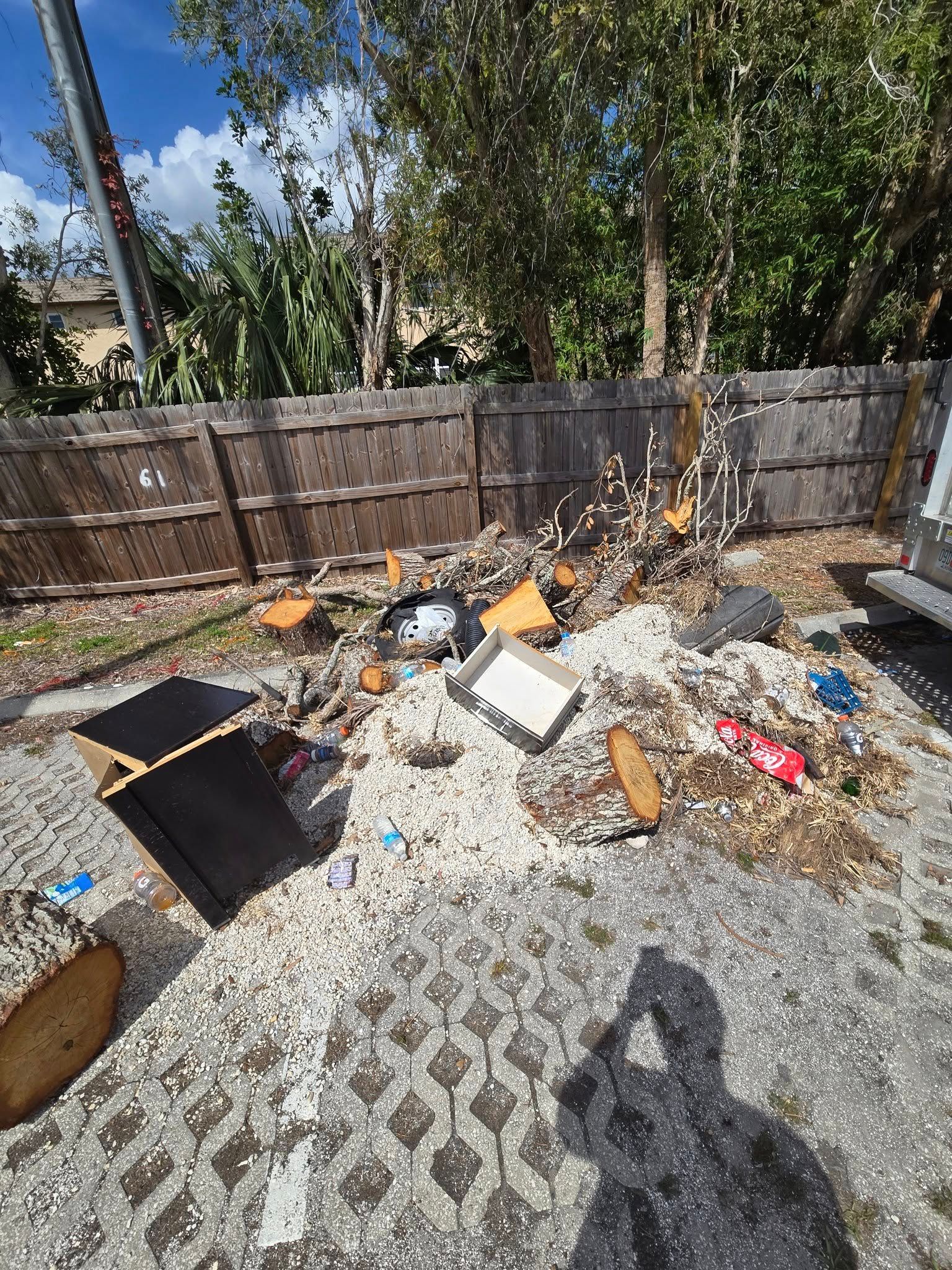 A pile of trash is sitting on the ground in front of a wooden fence.