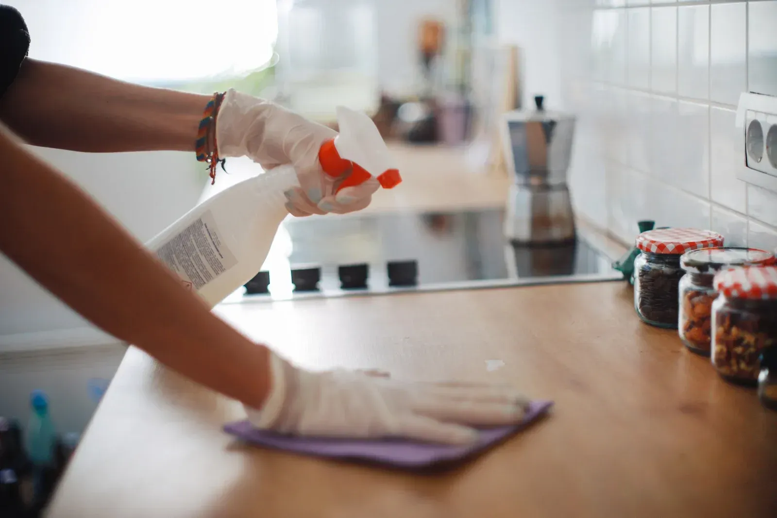 A person is cleaning a kitchen counter with a cloth and spray bottle.