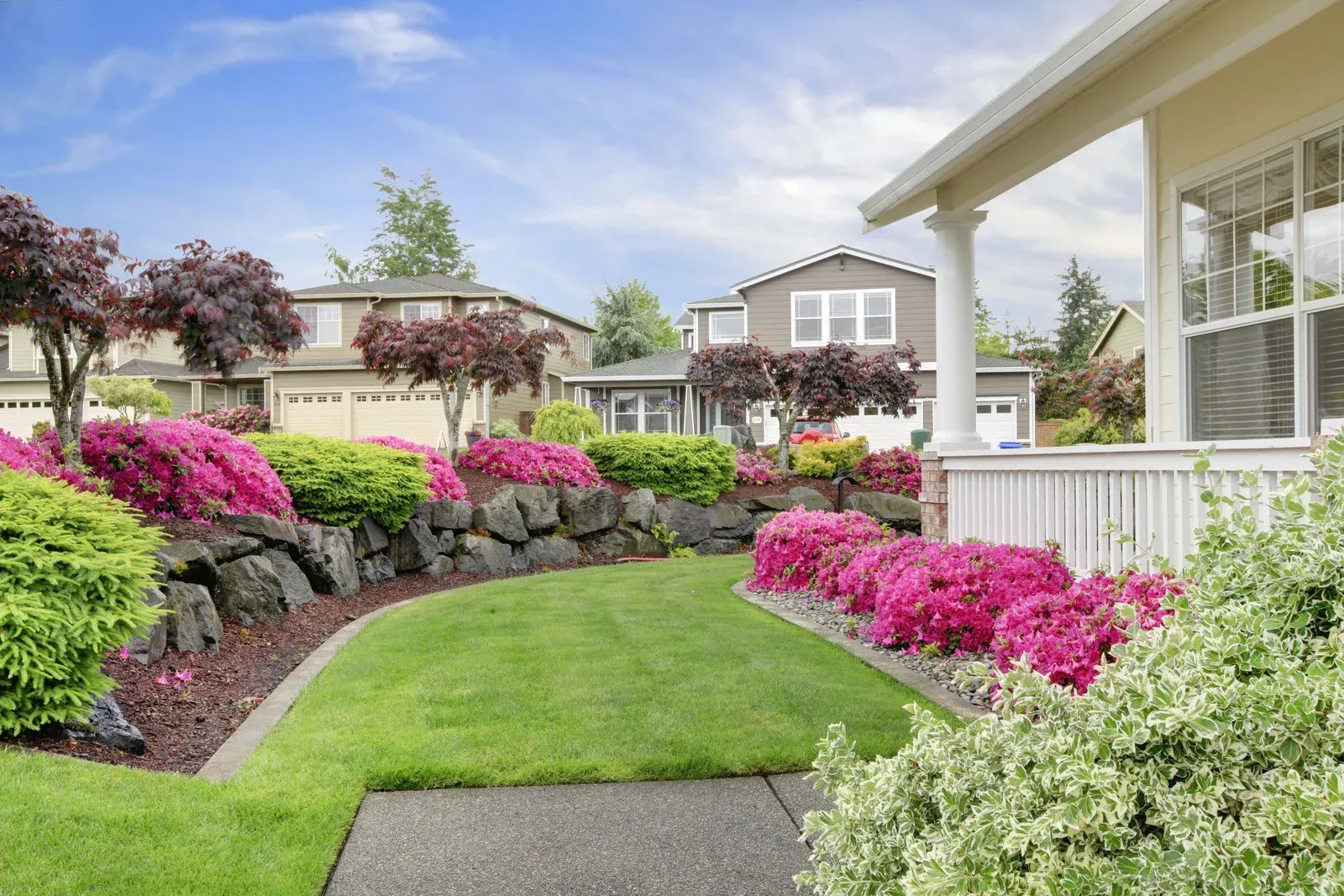 A house with a lush green lawn and pink flowers in front of it.
