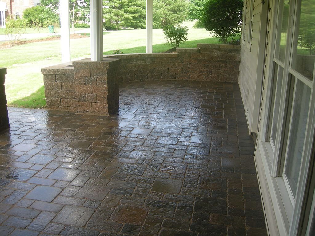 Wet brick patio with brown retaining wall, white columns and house siding.