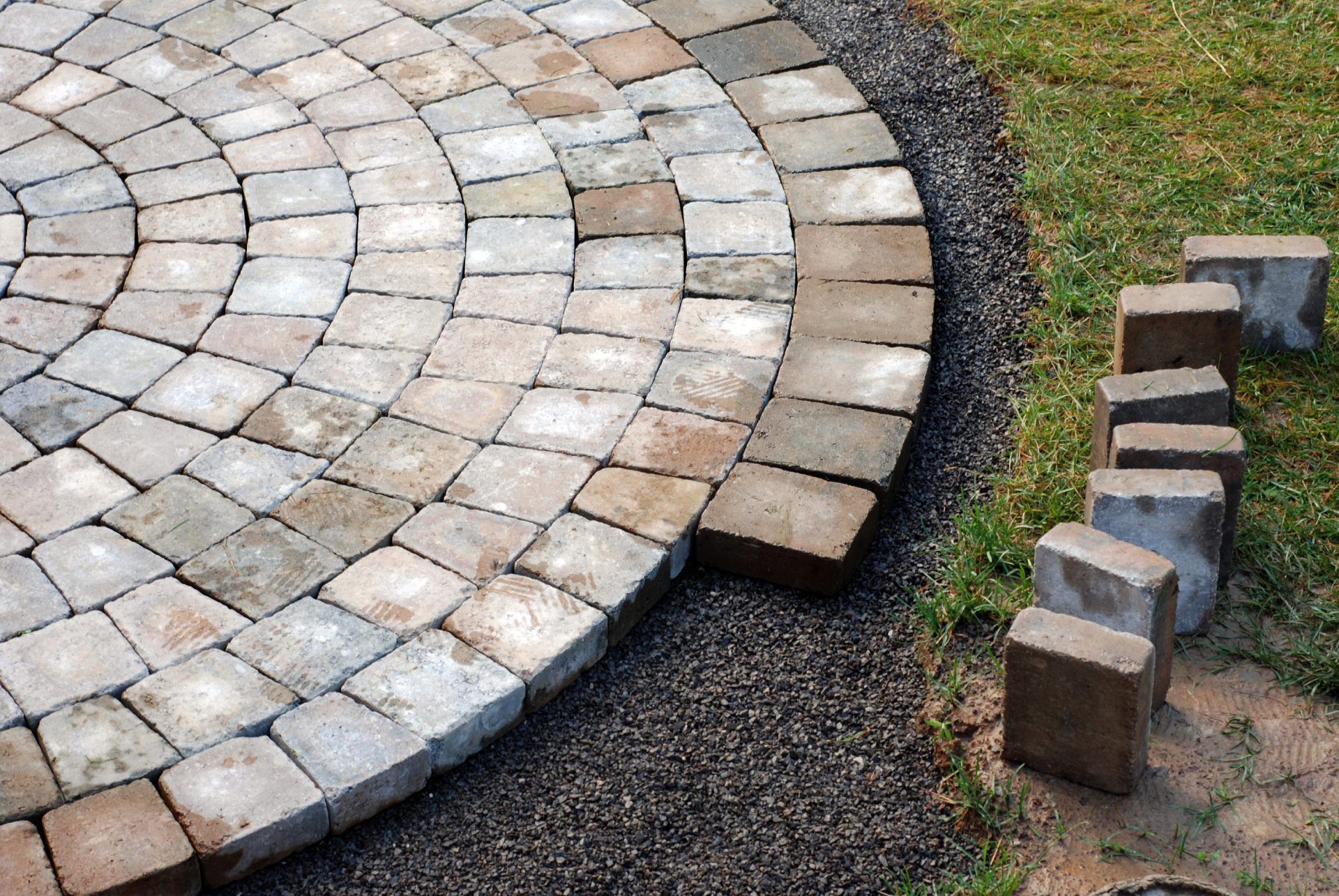 Circular stone patio with dark gravel border, adjacent to grass, with loose pavers nearby.