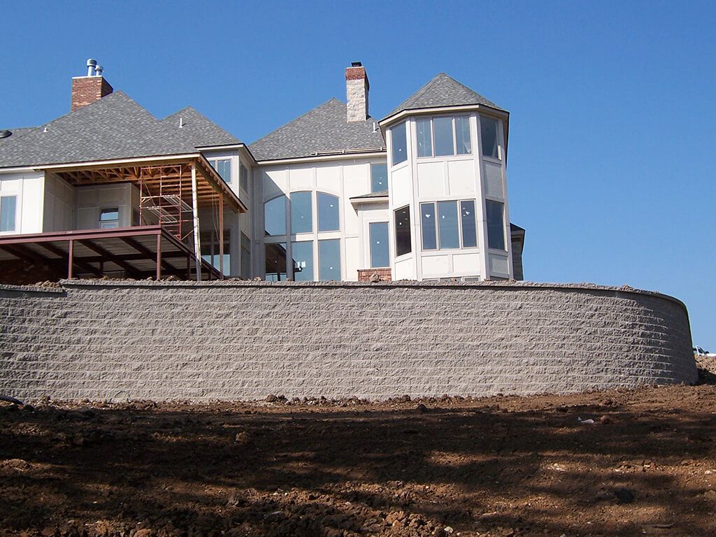 Large house on retaining wall. Gray block wall, white house, blue sky.