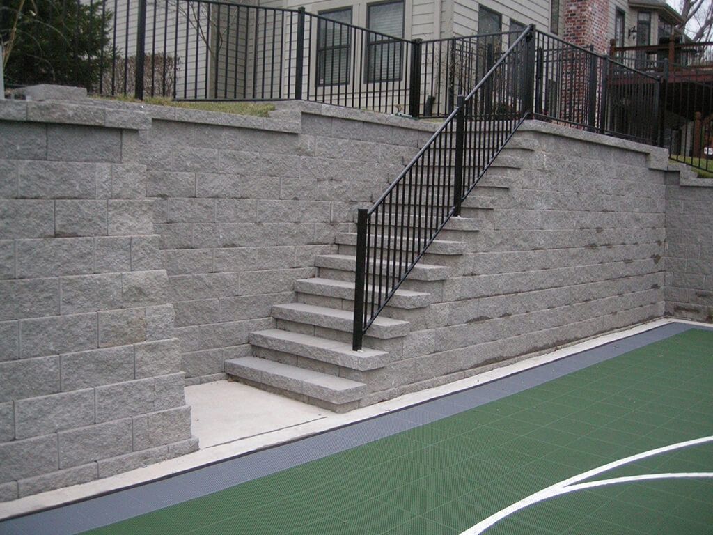 Brick retaining walls with stairs and a black handrail leading to a building.