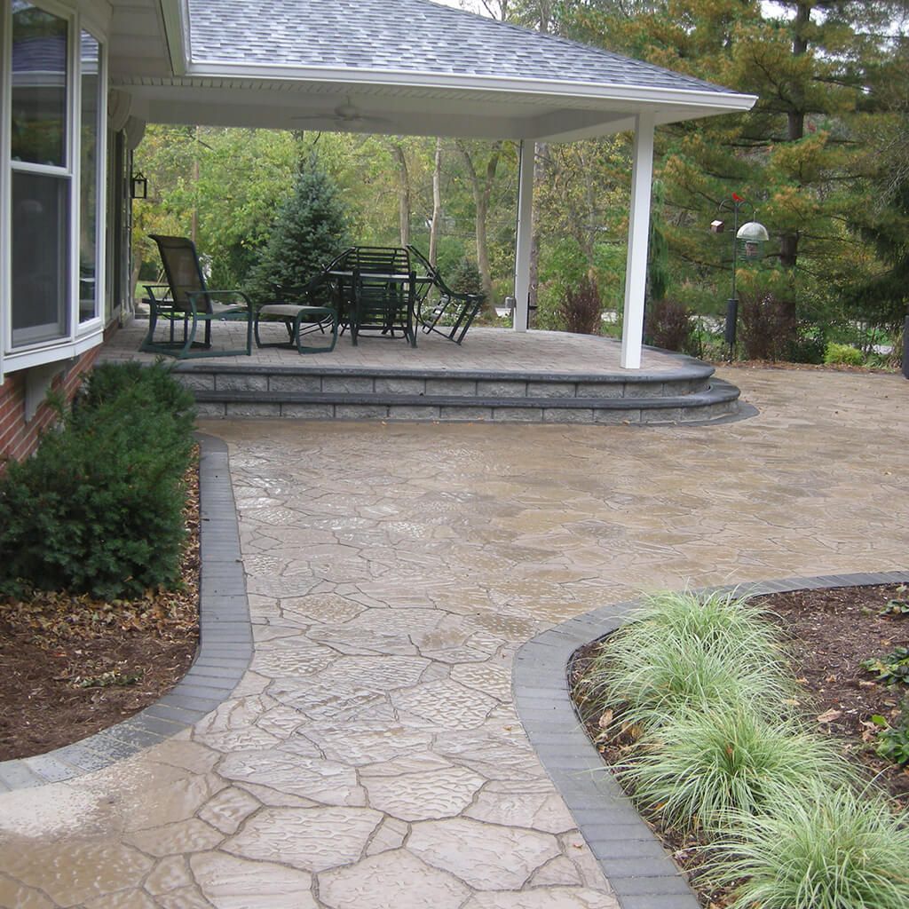 Stone patio with walkway leading to covered outdoor seating area. Green plants border the path.