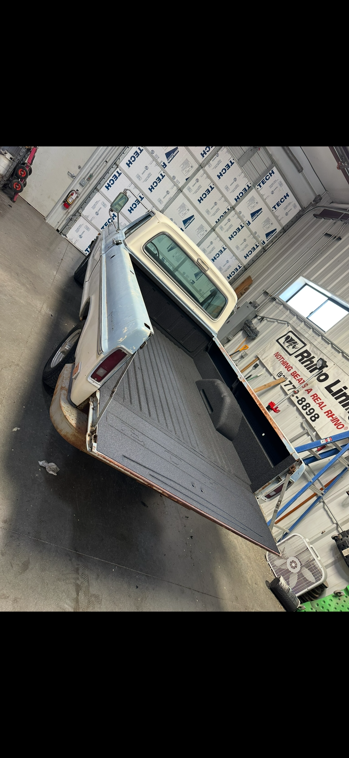 A beige pickup truck with the truck bed open, indoors.