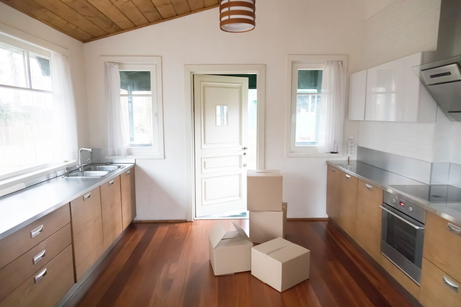 Empty modern kitchen with white cabinets, wood ceiling, and moving boxes on the floor