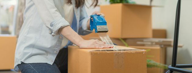 Person taping a cardboard box on a moving truck with packing boxes in the background
