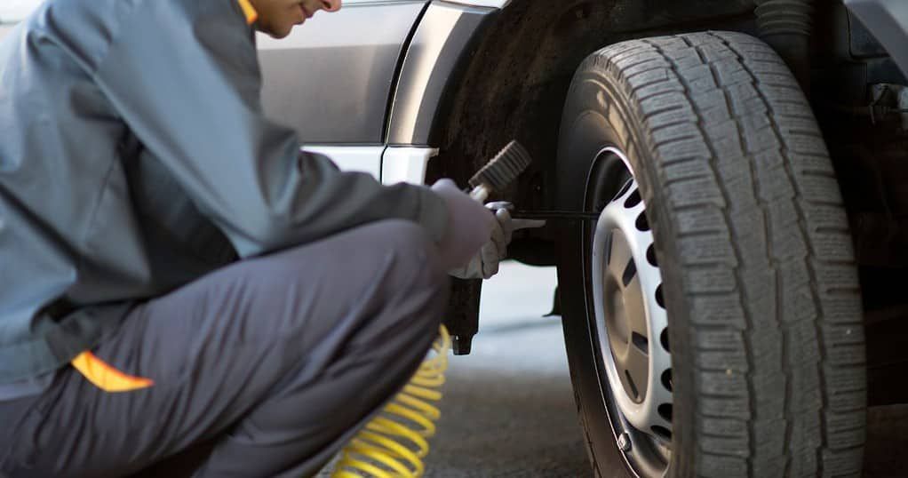 Person inflating a tire, next to a vehicle.