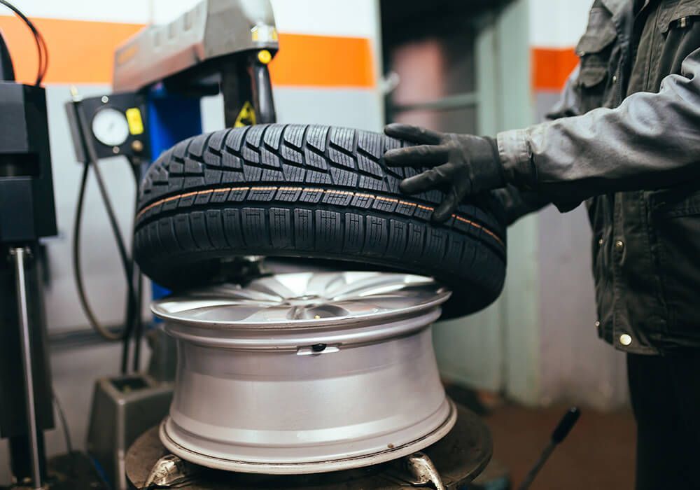 Mechanic mounting a new tire on a silver wheel in a garage.