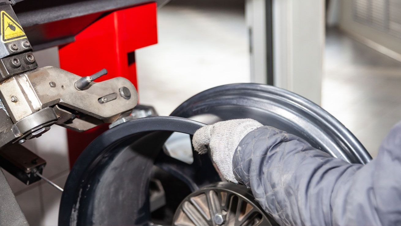 A person in a garage setting using a machine to work on a car wheel.