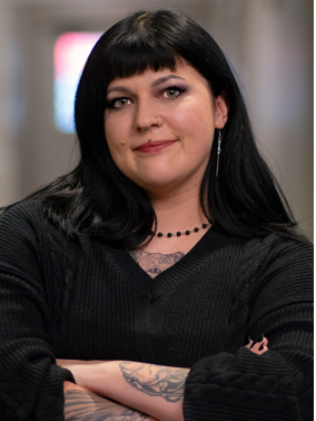 A woman wearing glasses and a pink jacket is standing in front of a tree.