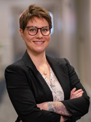 A woman wearing glasses and a black jacket smiles for the camera