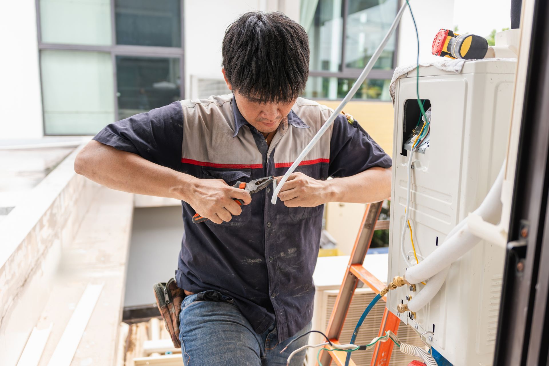 Technician cutting a white cable near an outdoor AC unit.