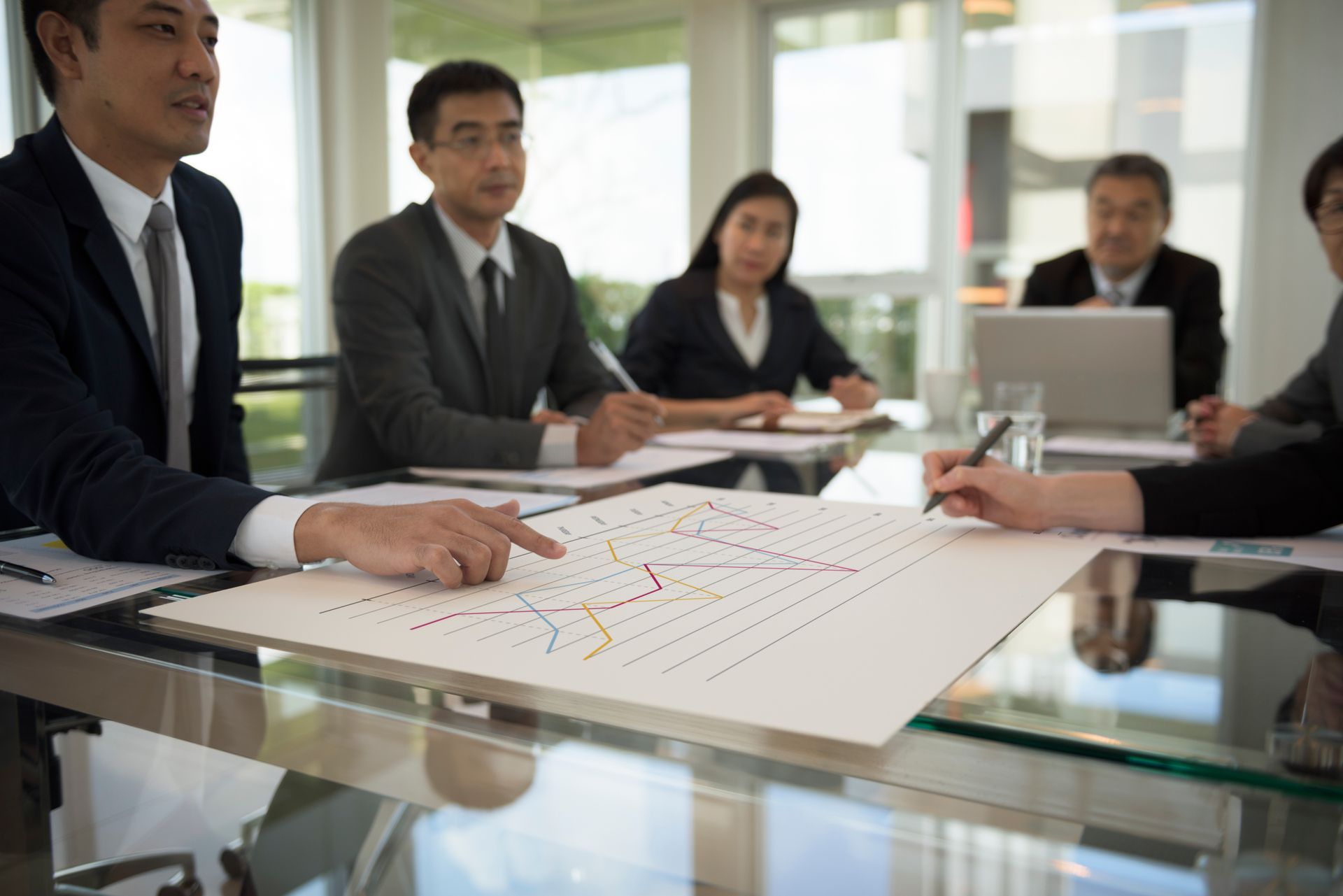 Business team meeting at a table, reviewing a graph. Man points at chart.